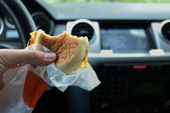 Closeup of a hand with a snack wrapped in a paper, concept of driving and eating