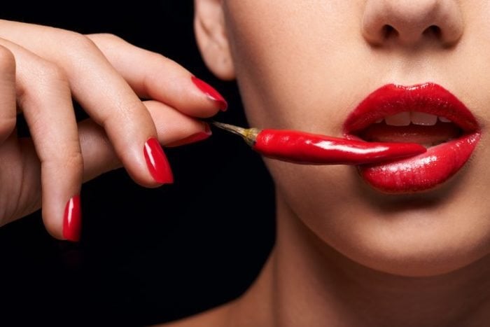 Closeup of a woman holding a red chilli to her mouth